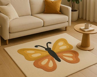 Puede incluir: Una alfombra rectangular beige con un gran diseño de mariposa en tonos amarillos, naranjas y negros. La mariposa tiene patrones de alas detallados. La alfombra está sobre un suelo de madera, con un sofá beige y una mesa auxiliar en el fondo.