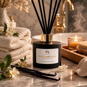 May include: A matte black cylindrical reed diffuser bottle with a gold collar and black reeds. The white label reads 6S Sixth Scents, Driftwood Crème, Sandalwood | Creamy Vanilla, Luxury Reed Diffuser | 200ml. It is surrounded by white flowers and vanilla beans.