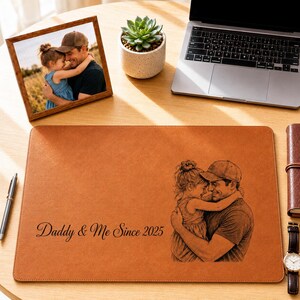 May include: A brown leather desk mat with a custom illustration of a father and child hugging. The text "Daddy & Me Since 2025" is printed on the mat. A framed photo and a succulent plant are also on the desk.