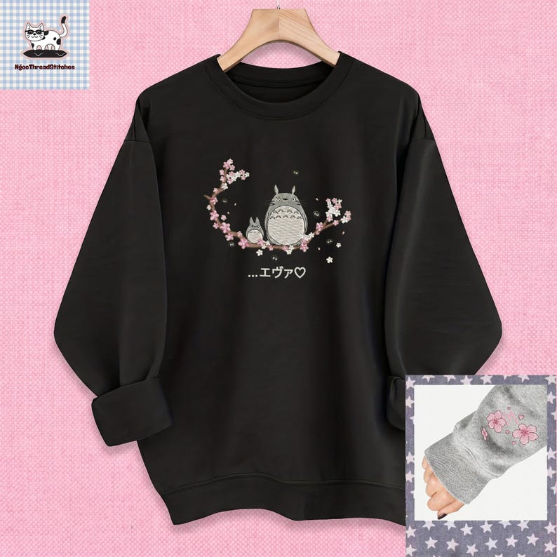 May include: Black sweatshirt with a crew neck and long sleeves. The front features an embroidered design of two cartoon characters and cherry blossoms. The text "...エヴァ♡" is below the characters. The sleeve cuff has a small embroidered cherry blossom design.