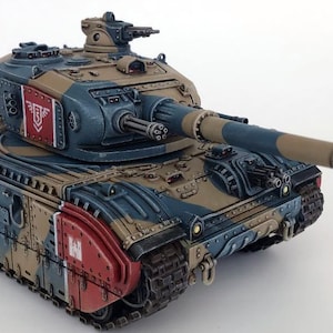 May include: A detailed model tank in shades of blue, tan, and red. The tank features a long barrel, multiple turrets, and intricate detailing. The model has a camouflage pattern and is likely a collectible or display item.