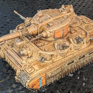 May include: A detailed model tank in shades of tan and brown, with visible rivets, a large cannon, and multiple turrets. The miniature military vehicle has orange and blue accents, and a weathered appearance.