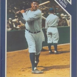 May include: Baseball card featuring Babe Ruth of the New York Yankees, in his pinstripe uniform, holding a bat. The card includes the text "BEATING THE ODDS" and the year 1927. The background shows a baseball field and other players.