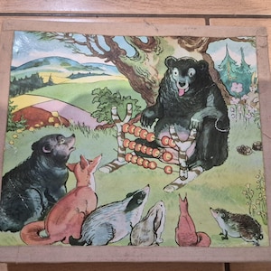May include: Vintage children's illustration featuring a black bear with a tongue out, using an abacus, surrounded by other forest animals. The scene is set in a green meadow with trees and hills in the background. The artwork is framed in a wooden border.