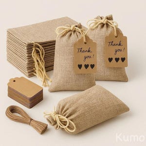 May include: A selection of burlap favour bags, tags, and twine. The bags are tied with string and have tags that read "Thank you!" with three heart symbols. A stack of tags and a bundle of twine are also present.