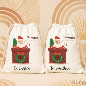 Puede incluir: Dos bolsas blancas con cordón con un diseño de Papá Noel. Cada bolsa presenta a Papá Noel en una chimenea, un árbol de Navidad verde y una corona. Las burbujas de texto dicen "Ho Ho Ho!" y las bolsas están etiquetadas "To: Lauren" y "To: Jonathan".