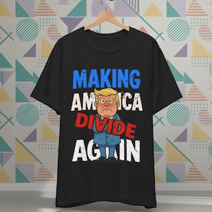 May include: Black t-shirt with the text "MAKING AMERICA DIVIDE AGAIN" in blue, white, and red. The shirt features a cartoon illustration of a man with a stern expression, wearing a blue suit and a yellow hairstyle.