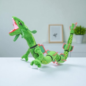May include: A green plush dragon toy with a long, serpentine body and a large head. The dragon has red accents on its wings and tail, with white claws and a pink mouth. The toy is posed on a white surface.