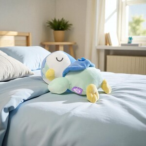 Puede incluir: Un peluche de p&aacute;jaro en tonos azules, verdes y amarillos descansa sobre una cama azul claro. El juguete tiene una cara sonriente y est&aacute; tumbado de lado. El fondo incluye una cama, almohadas, una ventana y una peque&ntilde;a mesa con una planta.