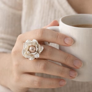 May include: A white ceramic mug with a black handle and the text "But First, Coffee" in a bold, black font. The mug is set against a blurred background, highlighting its clean design.