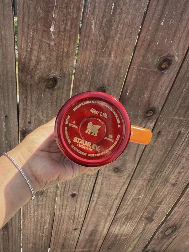 May include: A red Stanley brand tumbler base with a 40oz capacity, featuring a gold bear logo, the text 'DESIGNED IN SEATTLE WA', 'MANUFACTURED IN CHINA', 'BPA FREE', 'DISHWASHER SAFE', 'DO NOT MICROWAVE', and 'USING STRAW WITH HOT DRINKS MAY SCALD'.