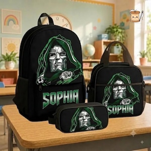 May include: A black backpack, lunch bag, and pencil case set featuring a graphic of a masked character in a green hood. Each item displays the name SOPHIA in bold green lettering below the character illustration. The set is made of black fabric.