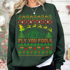 May include: Dark green sweatshirt with a festive design featuring a hobbit hole, reindeer, and the text "FLY YOU FOOLS" in orange. The design includes red, green, and yellow accents, creating a holiday-themed look.