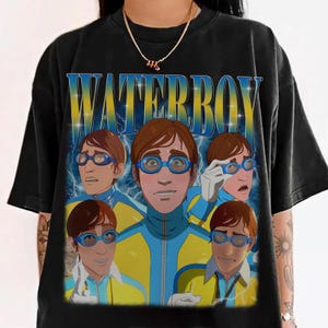 May include: Black t-shirt featuring a graphic of a person wearing blue goggles and a yellow and blue uniform, with the word "WATERBOY" in blue and yellow text. The design includes multiple images of the person with different facial expressions.