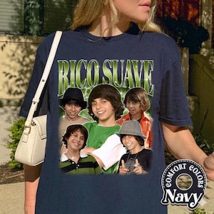 May include: Navy blue t-shirt featuring a graphic of a group of young men with the text "RICO SUAVE" in green. The shirt has a Comfort Colors label in the lower right corner. The design includes multiple images of the same person.