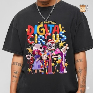 May include: A black short-sleeve t-shirt featuring a colorful graphic print with the text THE AMAZING DIGITAL CIRCUS. The design includes a group of animated characters in bright colors, surrounded by yellow stars and lightning bolt accents.