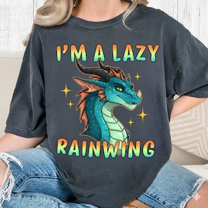 May include: Dark gray t-shirt featuring a teal and orange dragon illustration with the text "I'M A LAZY RAINWING". The dragon has black horns and is surrounded by yellow star accents. The shirt is a casual wear item.
