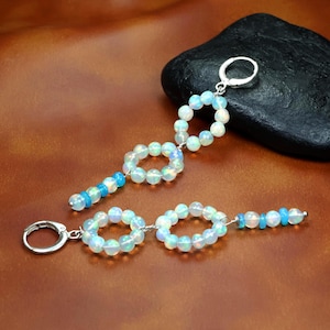 Könnte beinhalten: Ohrringe zum Hängen mit schillernden Opalperlen und silberfarbenem Metall. Die Ohrringe haben ein kreisförmiges Design mit einer Ansammlung von Perlen und blauen Perlenakzenten. Die Ohrringe werden auf einer braunen Oberfläche präsentiert.