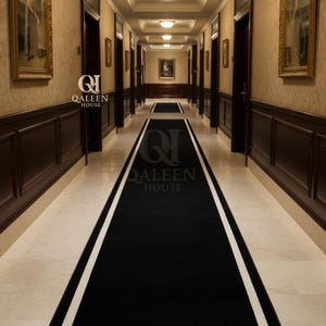 Op de afbeelding: Een lange gang met een zwart tapijt met een witte rand. De muren zijn beige met donkere houten lambrisering en ingelijste kunstwerken. Het plafond heeft inbouwspots. De tekst "QALEEN HOUSE" is zichtbaar op het tapijt.