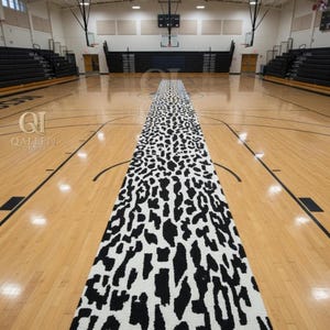May include: A long, rectangular rug with a black and white animal print pattern. The rug is placed in the center of a wooden basketball court. The court has black lines and bleachers on either side.