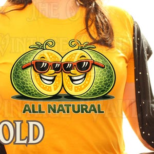 May include: Yellow t-shirt with a graphic of two smiling cantaloupes wearing sunglasses. The text "ALL NATURAL" is below the cantaloupes, and "GOLD" is at the bottom. A black and white polka dot sweater is draped over the shoulders.