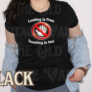 May include: Black t-shirt with the text "Looking Is Free. Touching Is Not." and a graphic of a hand inside a red circle with a line through it. The shirt is worn with a light blue denim jacket.