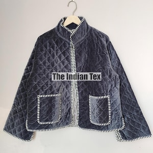 May include: A dark grey quilted jacket with a high collar, two front pockets, and a zip closure. The jacket features white and black striped trim and the text "The Indian Tex".