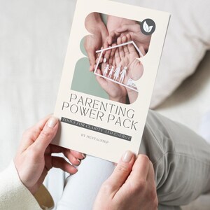May include: A cream-colored book titled "Parenting Power Pack" is held by a person. The cover features a family silhouette inside a house cutout, with hands in the background. The text "Tools for Clarity and Energy" is also visible.