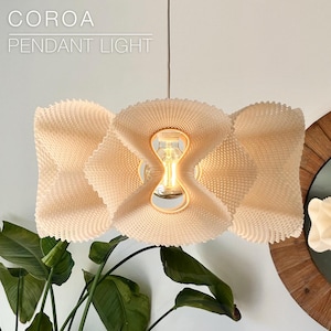 May include: A white pendant light with a complex, wavy, 3D-printed texture and a central opening revealing a glowing light bulb. The text COROA PENDANT LIGHT is visible in the upper left corner of the image, set against a plain white background.