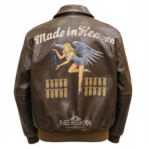 Könnte beinhalten: Braune Leder-Bomberjacke mit klassischem Kragen und gerippten Bündchen. Auf der Rückseite befindet sich ein gemaltes Design einer blonden Frau mit Engelsflügeln, die eine Bombe hält, mit dem Text "Made in Heaven" darüber und Reihen von Bomben darunter.