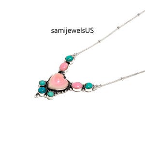 Puede incluir: Un collar de plata con un caboch&oacute;n central de concha rosa en forma de coraz&oacute;n, rodeado de piedras peque&ntilde;as redondas de color turquesa y ovaladas de color rosa en engastes de plata. El texto samijewelsUS se ve sobre el dije en la cadena.