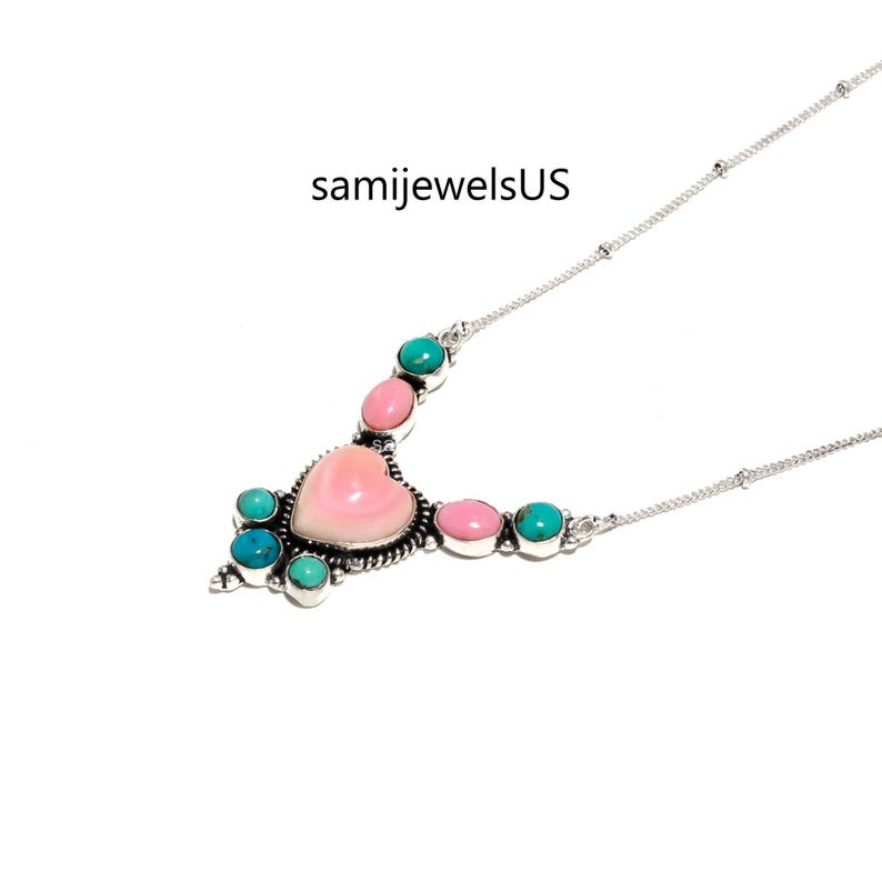 Puede incluir: Un collar de plata con un caboch&oacute;n central de concha rosa en forma de coraz&oacute;n, rodeado de piedras peque&ntilde;as redondas de color turquesa y ovaladas de color rosa en engastes de plata. El texto samijewelsUS se ve sobre el dije en la cadena.