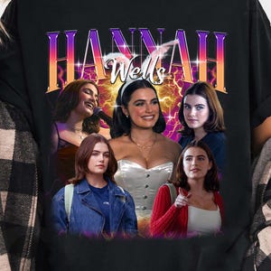 May include: A black t-shirt featuring a graphic print with the text "HANNAH Wells" in a purple and orange gradient font. The design includes a collage of five photographic portraits of a person in various outfits, set against a glowing yellow and purple background with lightning-like effects.