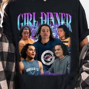 May include: A black t-shirt featuring the text "GIRL DINNER" in a purple and blue gradient font above a collage of four photographs of the same person with curly hair, wearing various shirts including one with "BRIAR U" text and a hawk logo.