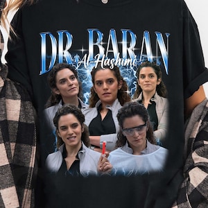 May include: Black long-sleeve t-shirt featuring a graphic of a woman with the text "DR. BARAN Al Hashimi" in a blue and white design. The graphic includes multiple images of the woman with a lightning bolt background.
