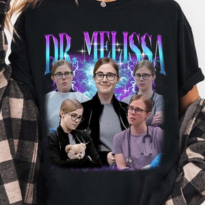 Może przedstawiać: Czarna koszulka z grafiką przedstawiającą osobę w okularach i napisem "DR. MELISSA" w stylu retro. Grafika zawiera wiele zdjęć osoby w różnych pozach, z fioletowo-niebieskim tłem błyskawic.