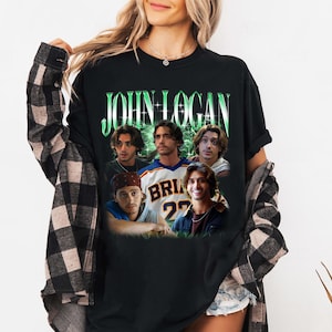 May include: A black t-shirt featuring the text JOHN LOGAN in a green font at the top, with a collage of five different photographs of the same person in various outfits and poses printed below the name against a green glowing background.