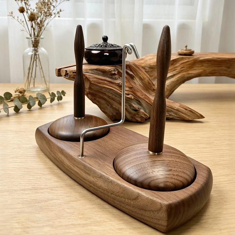 May include: A wooden yarn holder with two spindles and a metal yarn guide. The base is a rectangular shape with rounded edges. The spindles are dark brown with a brass accent at the base. The yarn holder is on a light brown wooden surface.