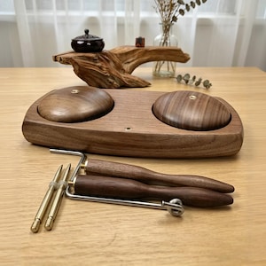 May include: A wooden tea set with two round lids, a small dark brown container, and tea utensils. The set is made of dark wood and has a natural, organic aesthetic. The utensils include a metal frame and wooden handles.