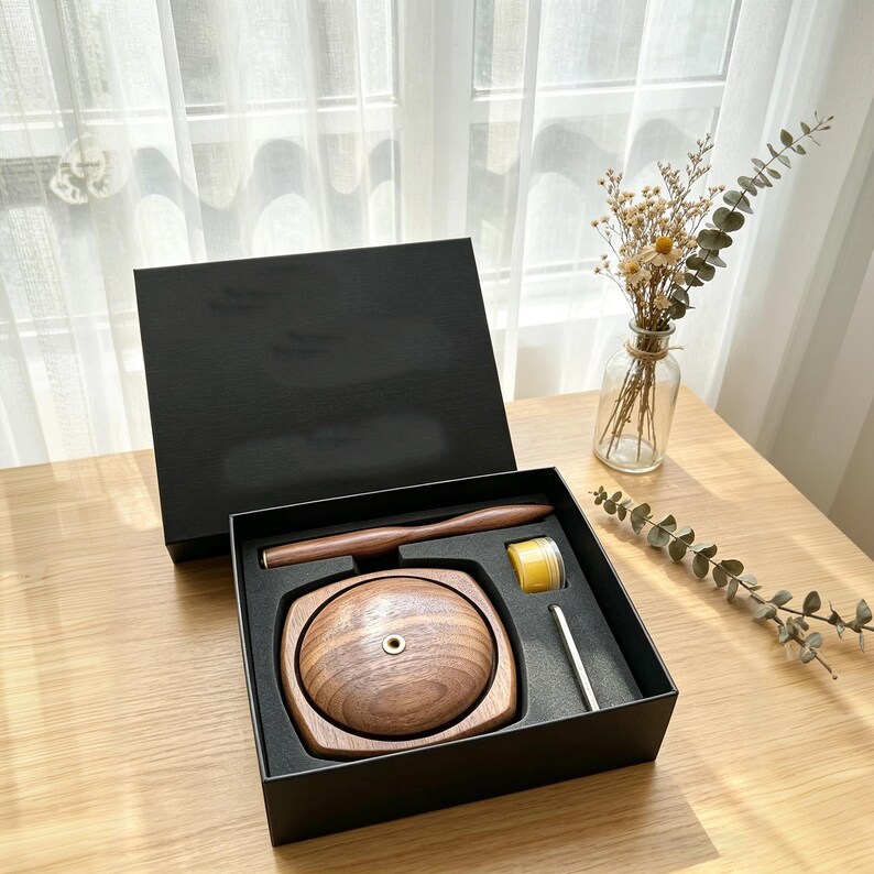 May include: A wooden incense burner set in a black box. The set includes a wooden incense holder, a wooden spoon, a small jar of yellow incense, and a metal tool. The incense burner is made of dark wood.