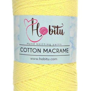 Op de afbeelding: Een gele bol katoenen macramé garen. Het etiket toont het "Hobitu" logo, de tekst "Hand knitting yarns" en "Cotton Macrame", en de website www.hobitu.com. Geschikt voor diverse handwerkprojecten.