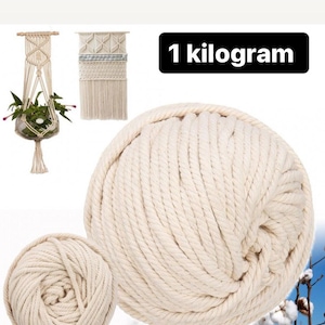 Puede incluir: Bola grande de cordón de macramé color crema, con una bola más pequeña delante. La imagen también muestra un colgador de plantas y un tapiz de pared de macramé. El texto "1 kilogramo" está en un rectángulo negro.