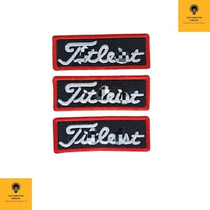 Peut inclure: Trois écussons rectangulaires noirs avec le mot "Titleist" en écriture blanche. Chaque écusson a une bordure rouge. Ces écussons sont probablement destinés aux vêtements ou aux accessoires.