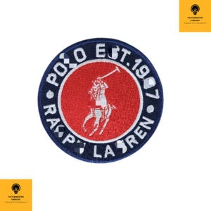 Może przedstawiać: Okrągła, haftowana naszywka z granatową obwódką i czerwonym środkiem. Projekt zawiera słowa "POLO EST. 1967 RALPH LAUREN" na krawędzi, otaczające białe logo gracza w polo.