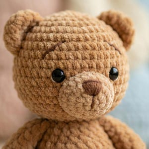 May include: Close-up of a handmade brown teddy bear. The bear has a textured, plush appearance with black eyes and a brown nose. The bear's ears are rounded, and the stitching is visible. This soft toy is perfect for children.