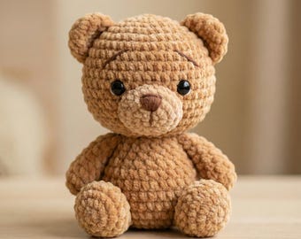 Könnte beinhalten: Ein handgefertigter, brauner Häkelteddybär mit schwarzen Sicherheitsaugen und einer kleinen braunen Nase. Der Bär hat ein strukturiertes, plüschiges Aussehen und sitzt aufrecht. Die Arme und Beine des Bären sind abgerundet.