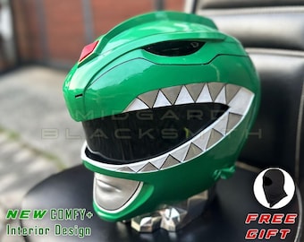 Op de afbeelding: Een glanzende groene helm met een donker getint vizier, een zilverkleurige mondplaat en een rij zilveren driehoekige tanden langs de rand van het vizier. Een kleine rode ruitvorm bevindt zich in het midden op het voorhoofd. De tekst Midgard Blacksmith is zichtbaar.