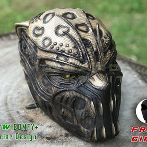 Op de afbeelding: Een gedetailleerd, getextureerd masker met een gevlekt patroon in tinten bruin en zwart, met een fel ontwerp. Het masker heeft een zwart onderste gedeelte met scherpe tanden en de tekst "NEW COMFY+ Interior Design" is zichtbaar. Een gratis cadeau is ook inbegrepen.