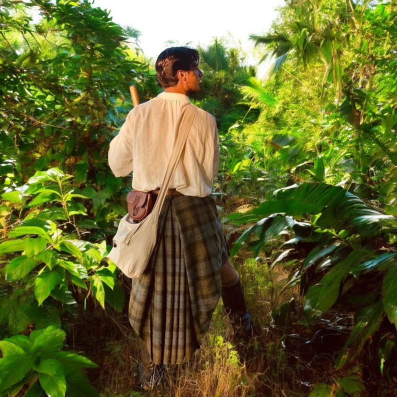 May include: A white long-sleeved shirt paired with a pleated plaid kilt in shades of grey, brown, and blue. A light-coloured canvas crossbody bag with a small brown leather pouch attached is worn over the shoulder, and a wooden staff is held in one hand.