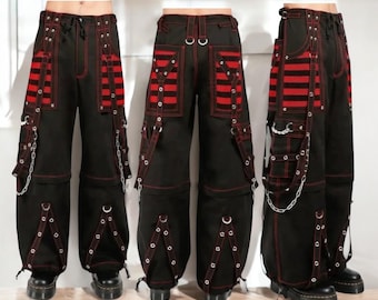 May include: Black cargo trousers with red detailing, including pockets, straps, and silver chain embellishments. The trousers have red stitching and a drawstring waist. The design incorporates red and black striped panels.